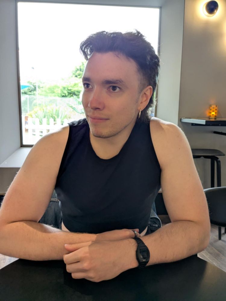 Me, a young white man wearing a black crop top and silver hoop earrings