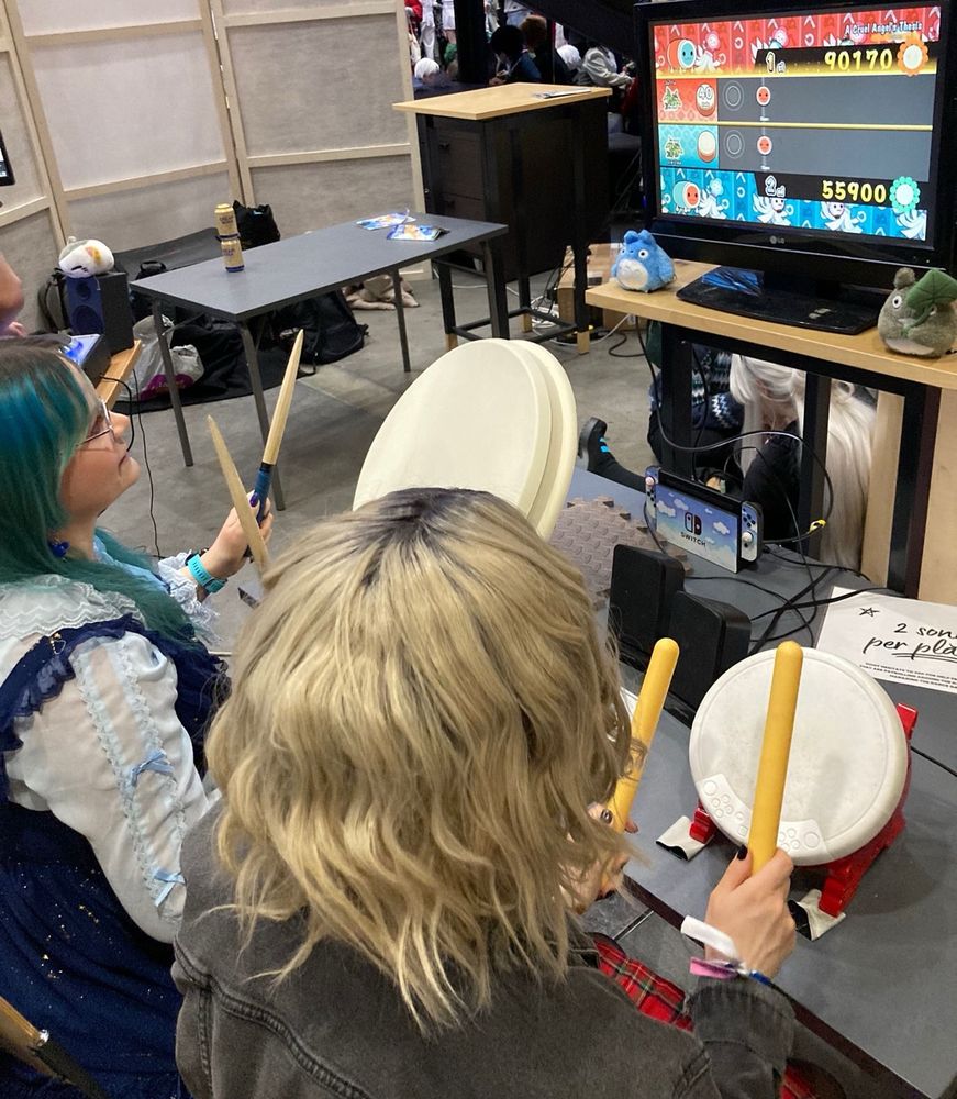 Apila in blue lolita style dress playing Taiko Drums rythm game on Nintendo Switch with Pauliina in Lila cosplay. 