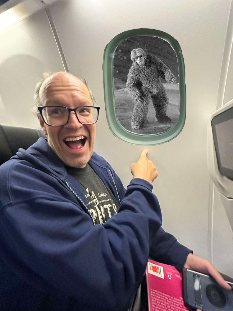 A happy man pointing out of a plane window at the gremlin from "Nightmare at 20,000 feet"