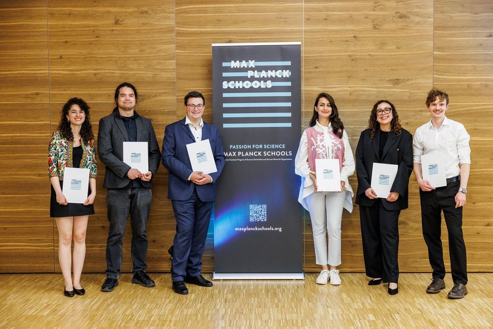 Graduates of the Max Planck Schools holding certificates next to a banner