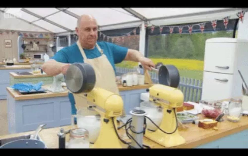 a man in an apron is standing next to two yellow mixers