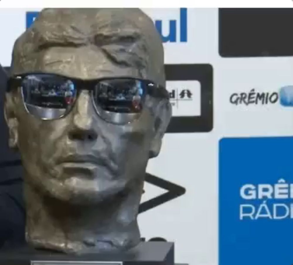 a statue of a man wearing sunglasses stands in front of a gremio logo