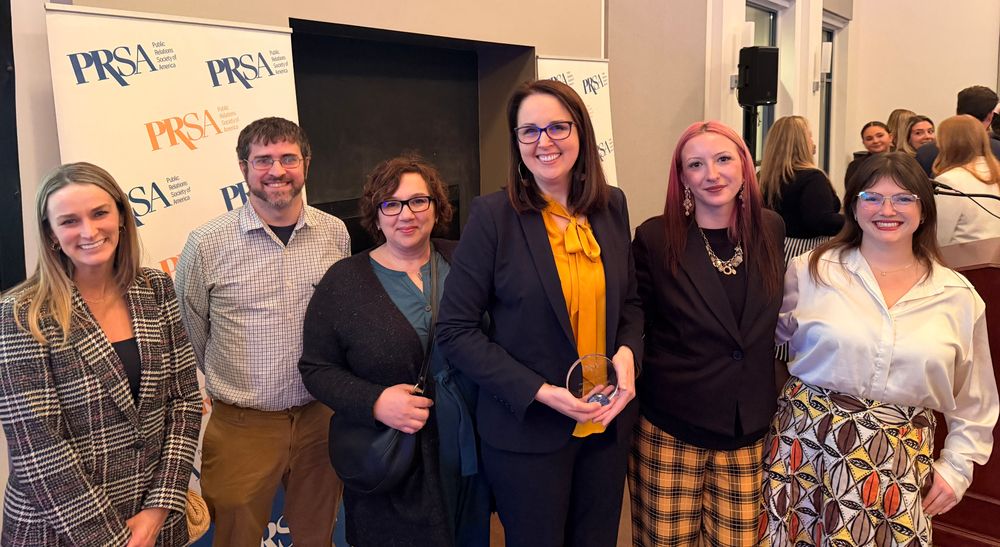 Five women and a man stand for a posed photo in front of a PRSA banner