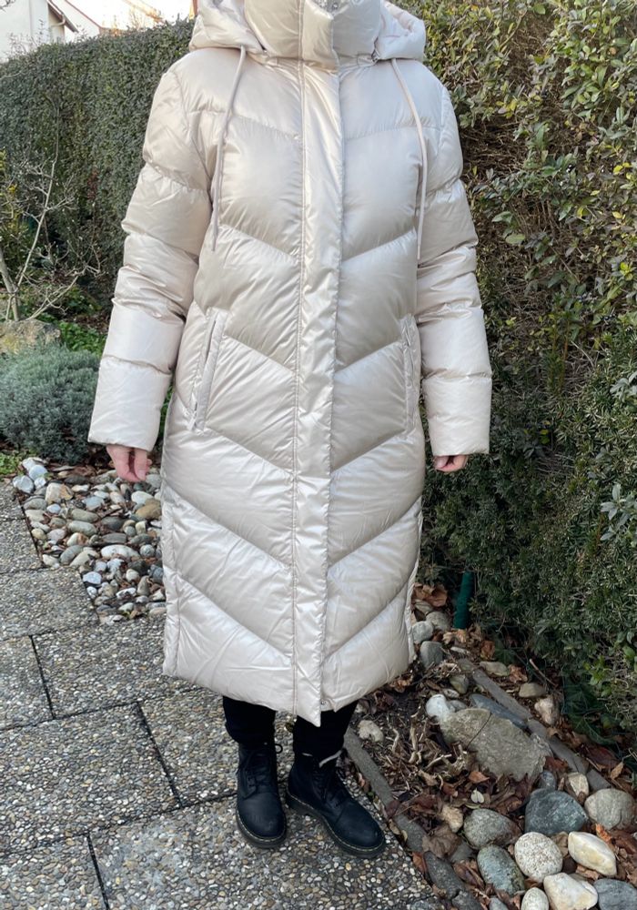 Aufnahme einer Frau (ohne Kopf) in einem cremefarbenen langen Steppmantel. Ich trage eine schwarze Hose und schwarze Winter Doc Martens