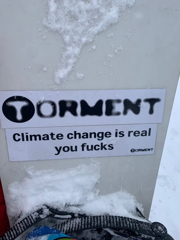 Some stickers on a snowboard that say TORMENT and Climate Change Is Real You Fucks