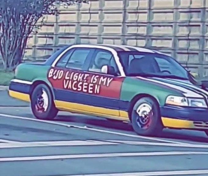 An older Crown Victoria painted Rasta colors with white lettering that says BUD LIGHT IS MY VACSEEN