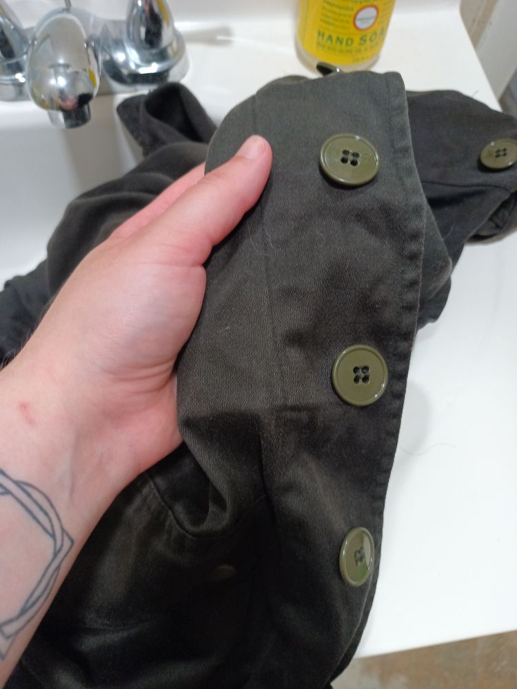 Closeup photo of my hand holding the button closure area of an old jacket, soaking wet from being in a tea dye bath all day.