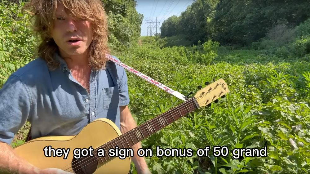 Singer Jesse Welles standing in a transmission line easement, singing "Join Ice". Lyrics: "they got a sign on bonus of 50 grand"