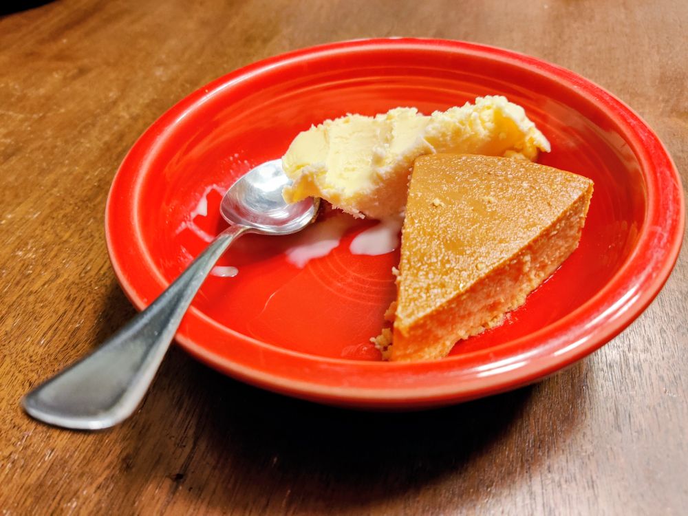 A slice of sweet potato flan in a red, ceramic bowl next to a scoop of ice cream.