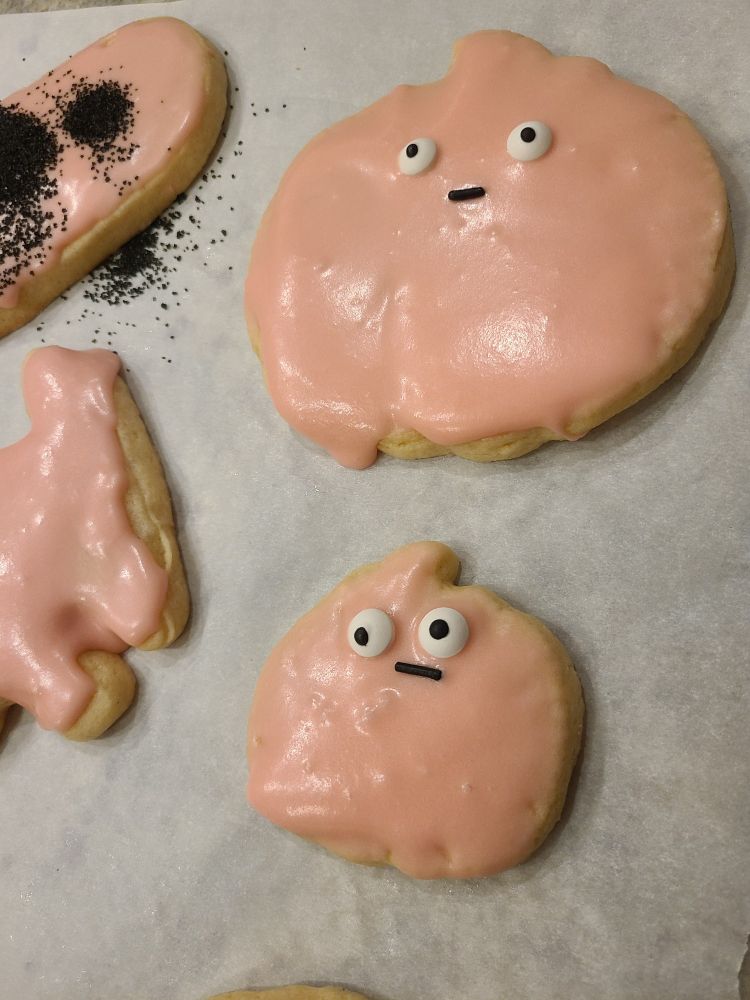 Pink Halloween cookies with candy googly eyes and a single black sprinkle as a mouth. They look worried.