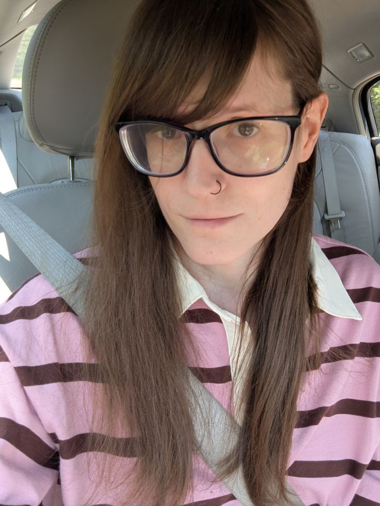 Picture of me a girl with long brown heair, a black nose ring, glasses, wearing a pink with brown stripes rugby shirt 