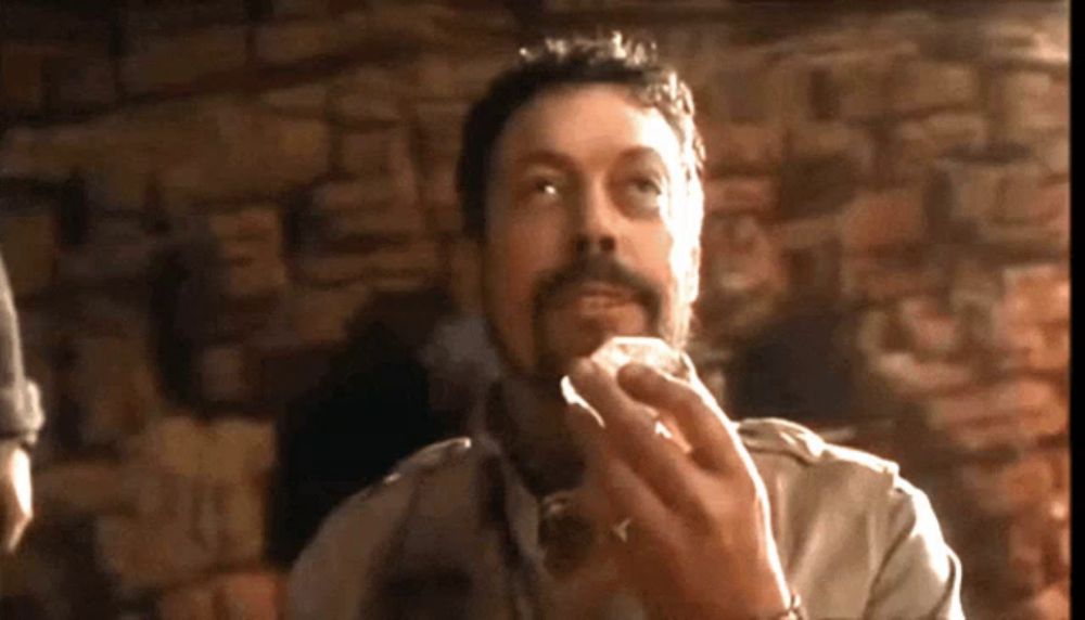 a man with a beard is eating something in front of a stone wall