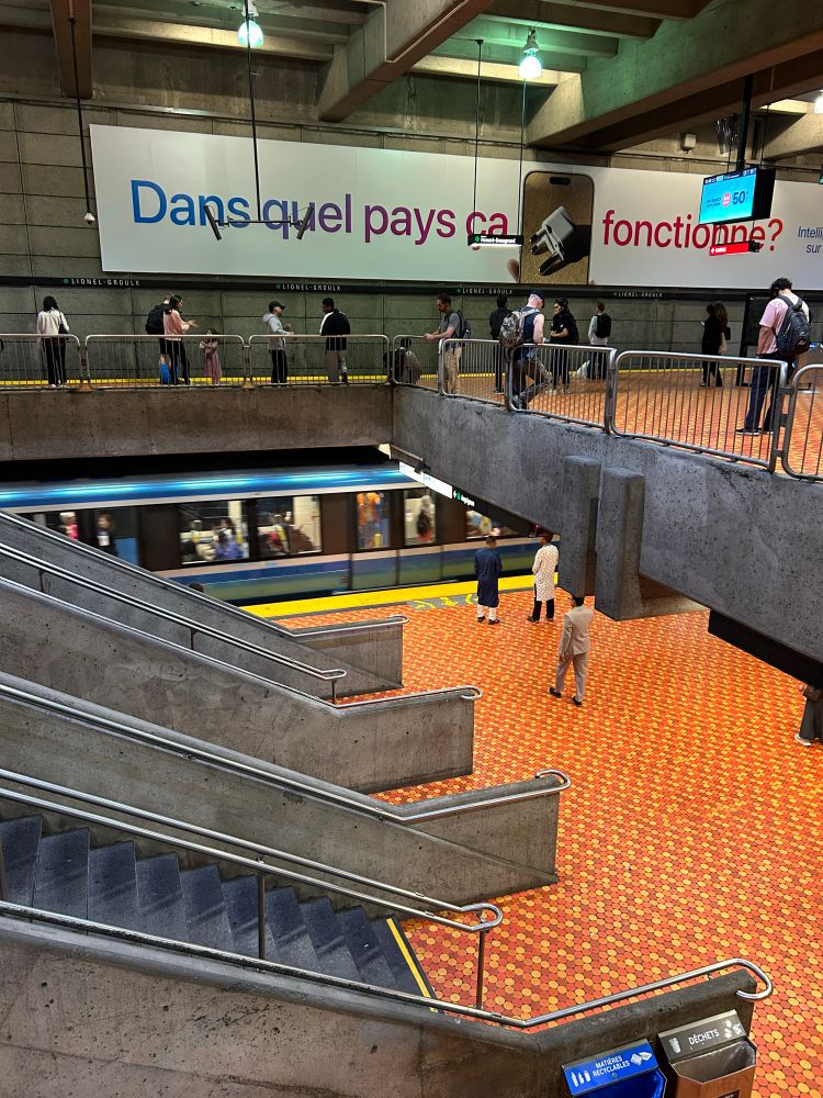 Looking town from an upper track to a lower track in a Métro station with cool multi-hued orange circular tiles. A train is pulling in on the lower track