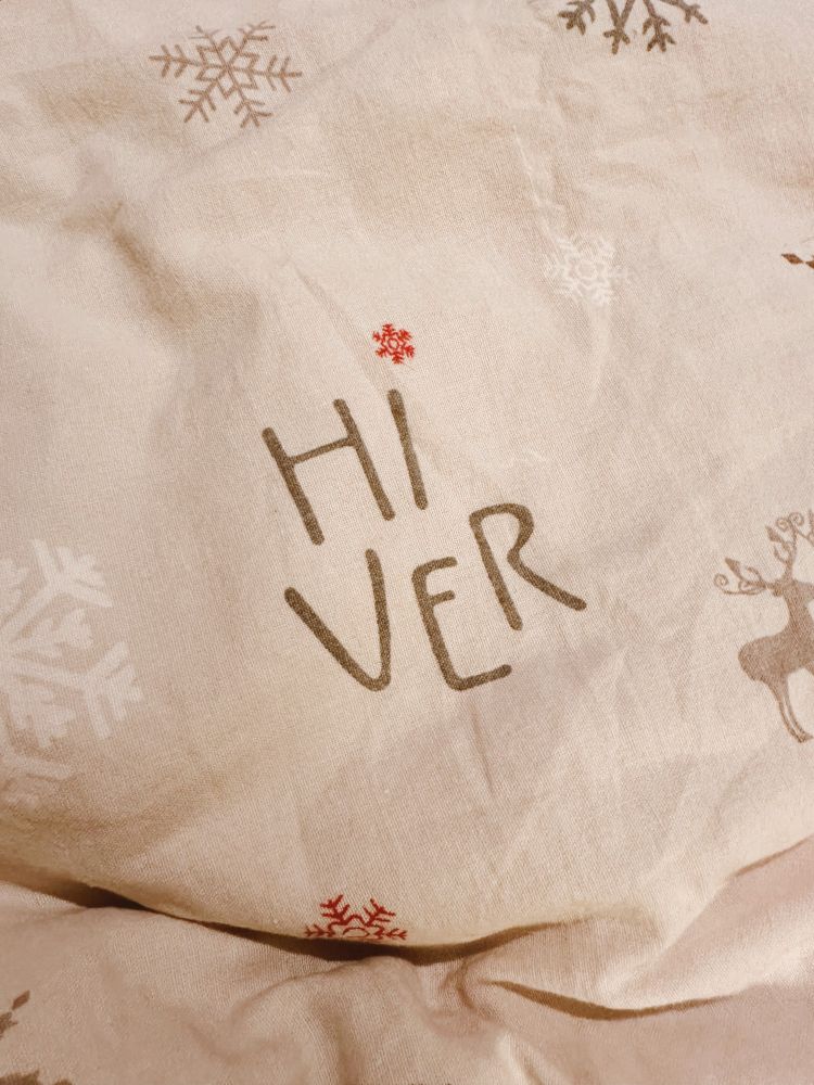Parure de lit crème sur laquelle il y a des flocons de neige, des petits rennes et l’écriture « Hi » puis saut à la ligne « Ver ».