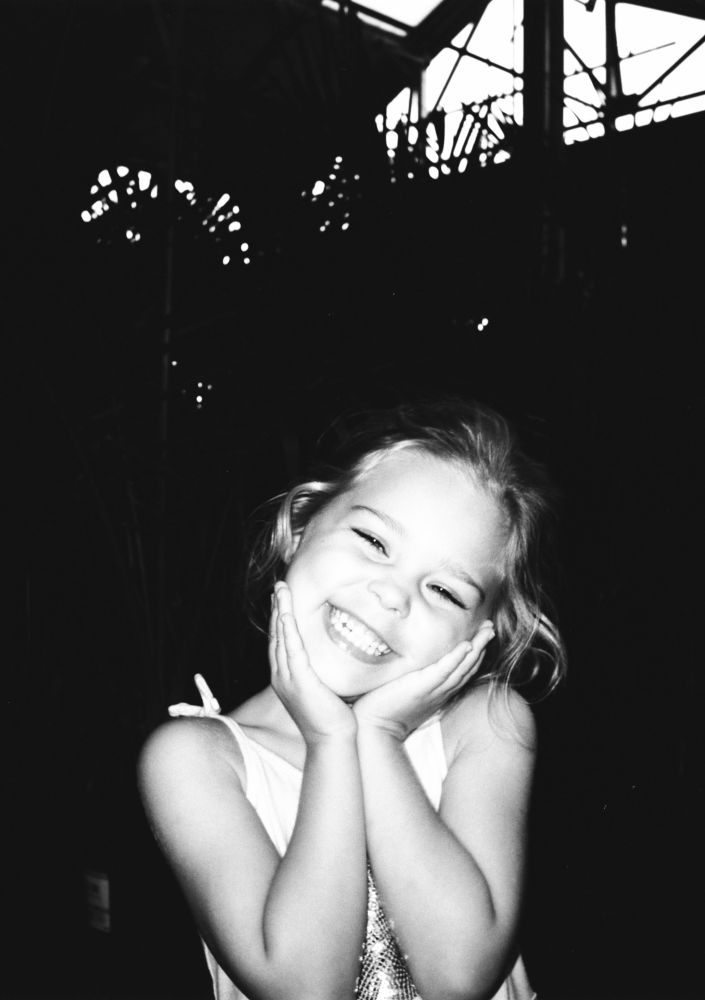 A young girl smiling with her head in her hands. Black and white film photo