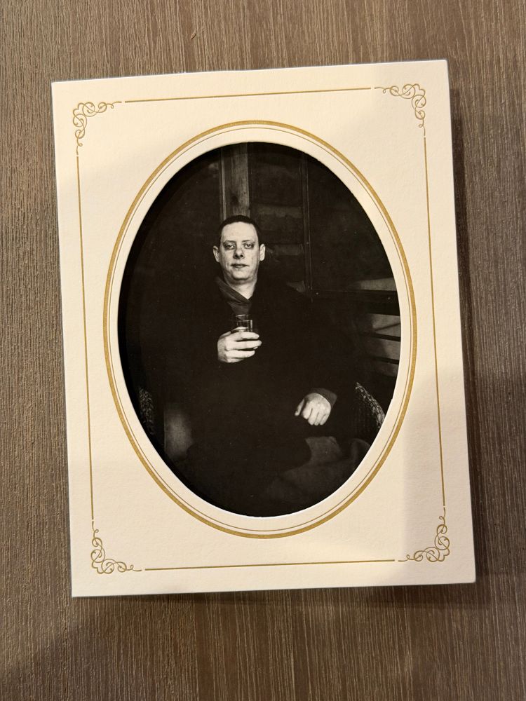 A black and white portrait of a man holding a glass. The photo is in an oval paper frame. 