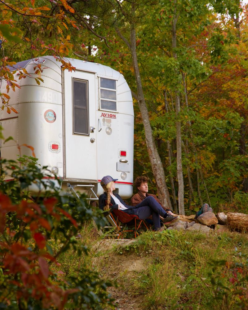 Man and woman sitting outside. Next to a truck camper. 
