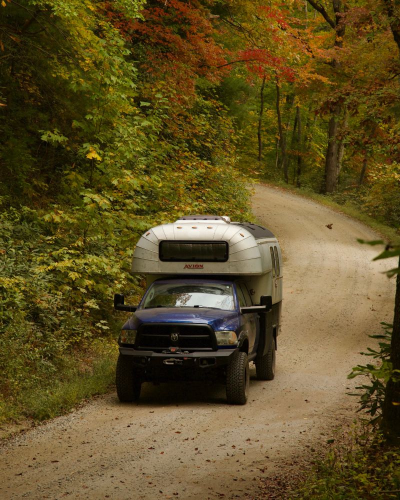 Vintage truck camper driving down a dirt road in fall