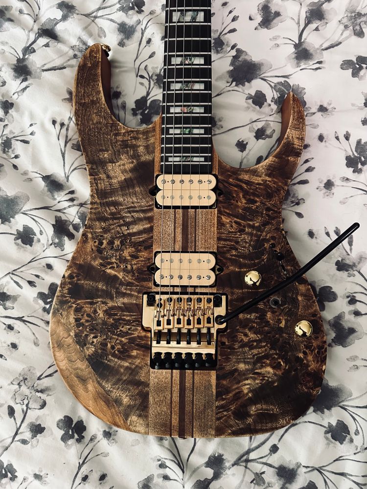 A photo of an Ibanez RGT1220PB-ABS, a brown s-style guitar with gold hardware