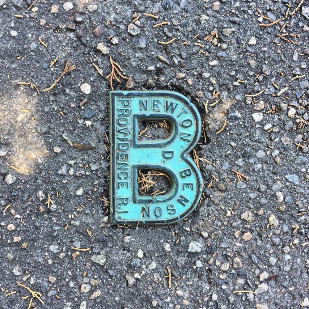 brass marker in the shape of a B, set in concrete, with words inside: Newton D Benson, Providence R.I.