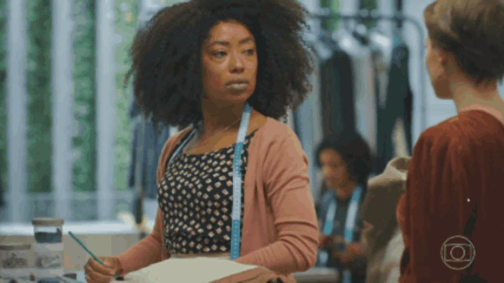 a woman in a pink cardigan with a measuring tape around her neck is talking to another woman