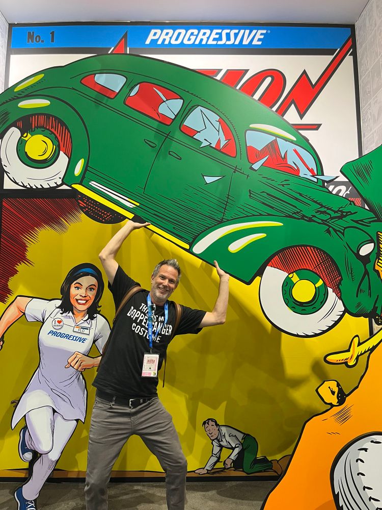 Adam recreating the front cover of Action Comics #1 at a display at Comic-Con, lifting a car in the air like Superman 