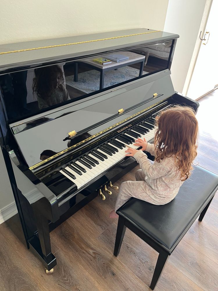 Black upright Baldwin piano being played by my three-year-old daughter