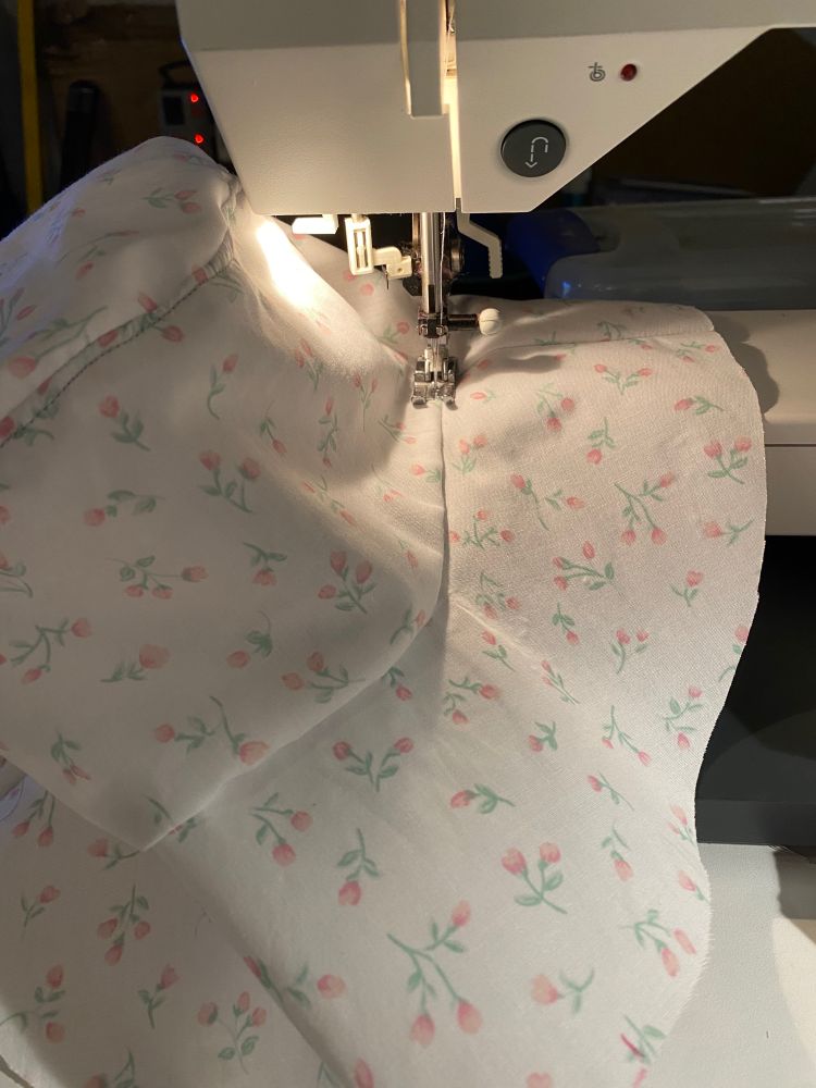 A white hat with small pink flowers under the needle of a sewing machine. This is the liner fabric