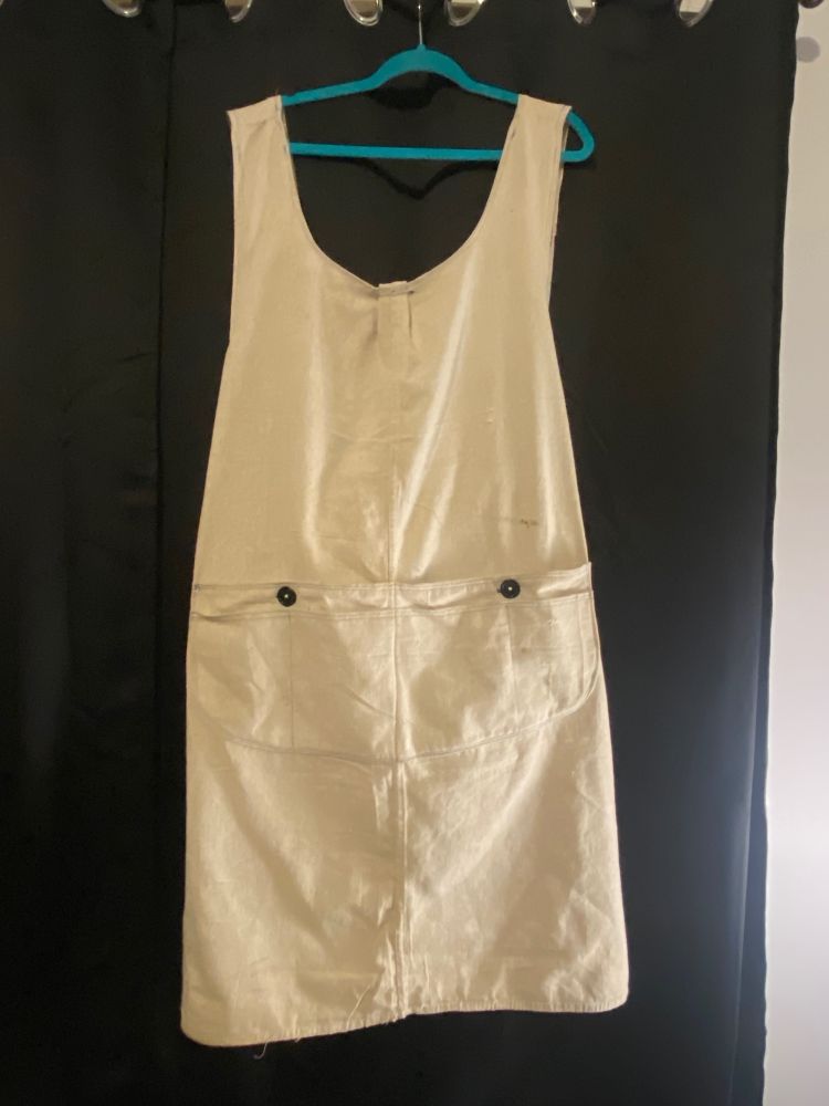 Picture of the entire utility apron hanging against black curtains on a teal hanger