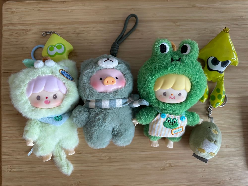 six blind box toys on a wood top table. every toy is from a different blind box set and all of them are predominantly green. 