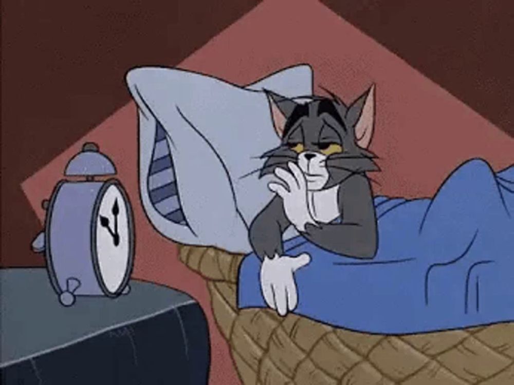 a cartoon cat is laying in bed with a pillow and an alarm clock .