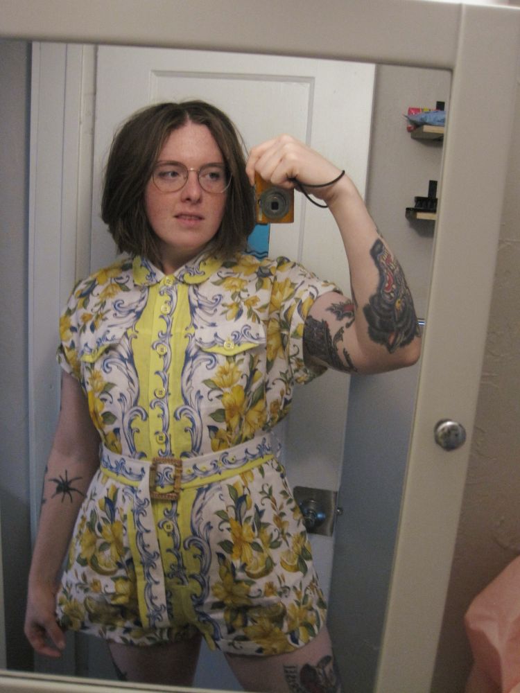 Bathroom mirror selfie of Nessie wearing a yellow Italian pattern, romper with flowers and lemons and these blue nautical swooshes