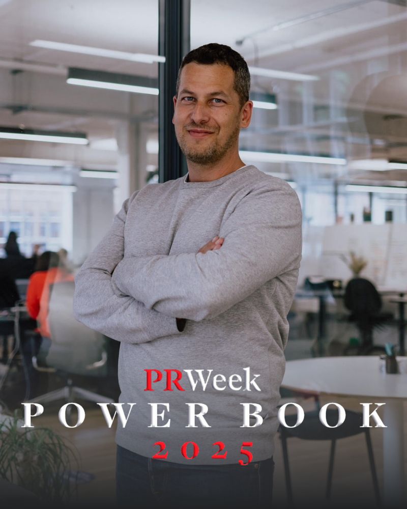 A dark-haired man wearing a grey jumper has his arms crossed and poses for the camera. Overlaid text reads PRWeek Power Book 2025.