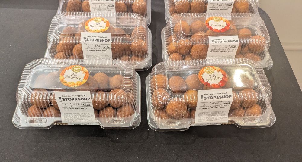 plastic containers of donut holes, half of which are apple cider flavor and half of which are pumpkin flavor. they have stickers on top proclaiming them to be "fall favorites"