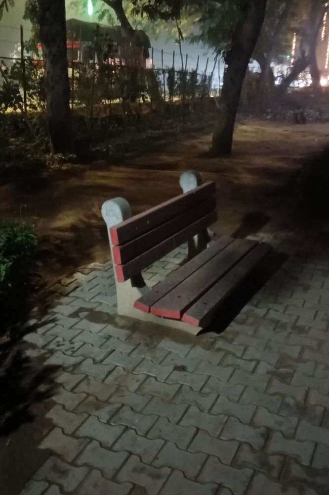 A picture of a park bench at night. The bench appears to be sunken into the brick ground.