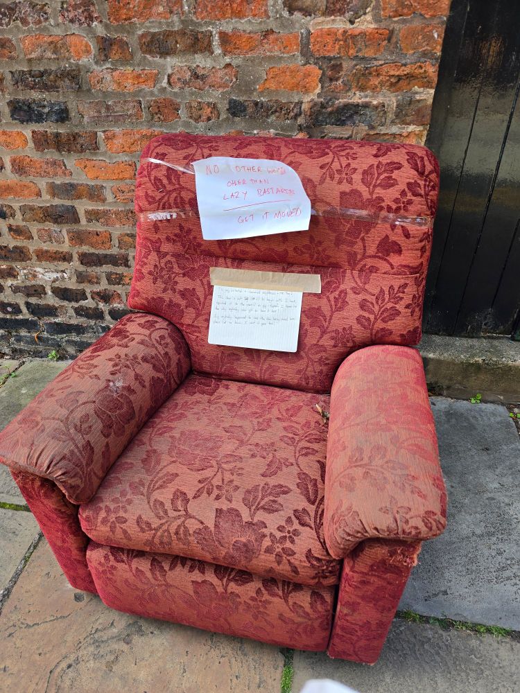 A dumped dark orange pink fabric armchair outside a house

2 handwritten paper notes sellotaped to it

1 a long apology from the house resident saying it was dumped outside their house; they've contacted the council, they dont like it and dont know what to do with it either

2nd "NO OTHER WORDS OTHER THAN LAZY BASTARDS - GET IT MOVED"