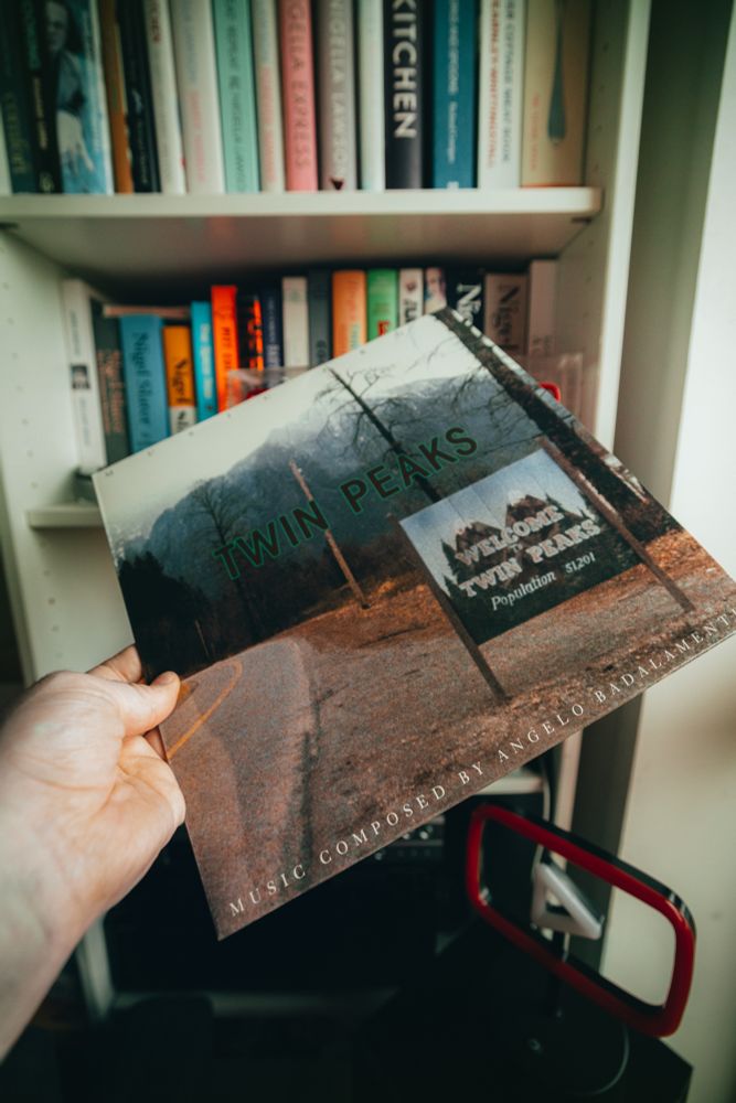 Me holding the album cover for the Twin Peaks OST on vinyl in front of a bookshelf