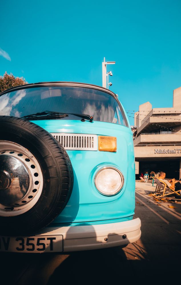 A VW van in cyan sits under an equally bright blue sky with the national theater. behind it.
