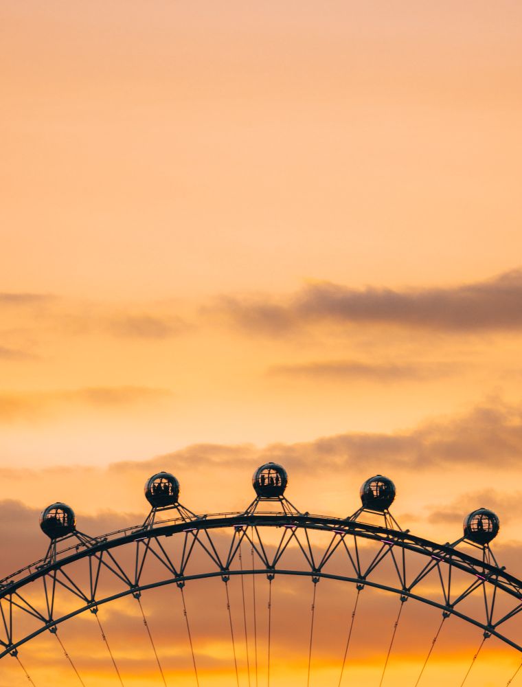 People silhouetted in the pods of the London eye against an orange sunset.