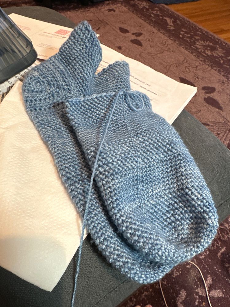 Two blue crocheted booty socks, one partially finished.