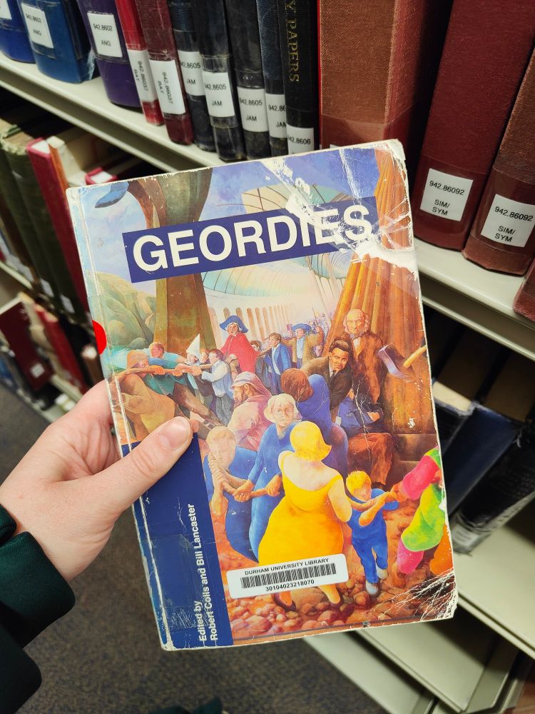 Image of a book in front of a bookshelf. It is "Geordies" by Robert Colls and Bill Lancaster. The front cover features a drawing of a variety of people, most of whom are pulling a rope. 
