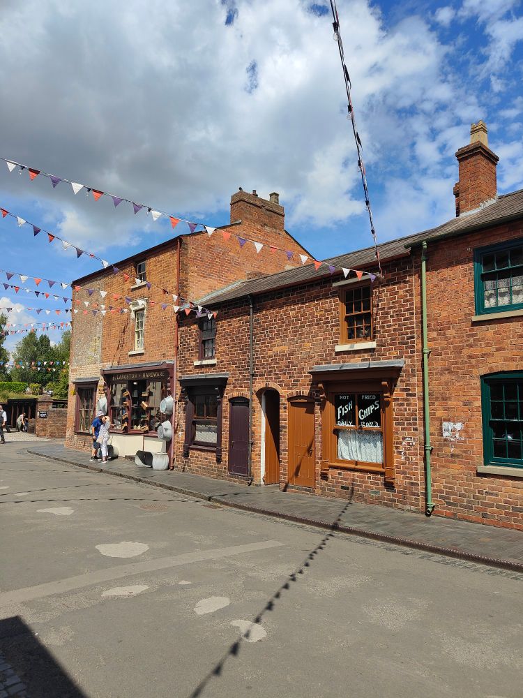 A view of a street of brick buildings at the black country living museum, with red white and blue bunting across the street 