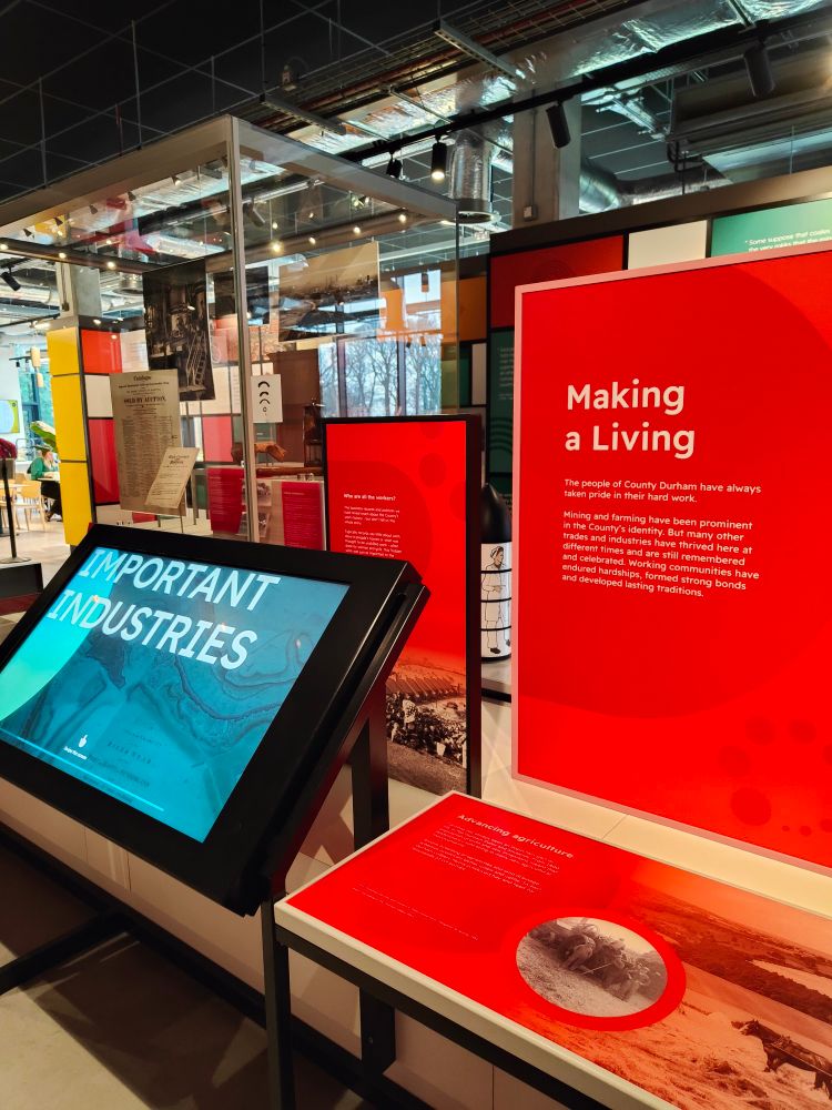 Museum display of important industries anf making a living, red panel with white text and interactive screen 