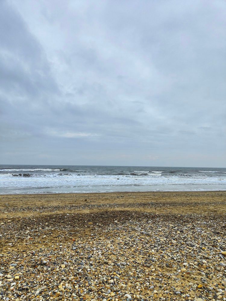 View from Seaham beach of the pebbled beach, receding tide and horizon and grey sky. 
