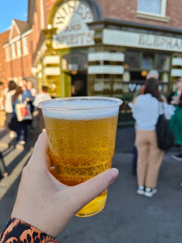 A pint of scrumpy cider held in front of a pub with green and cream tiled frontage 