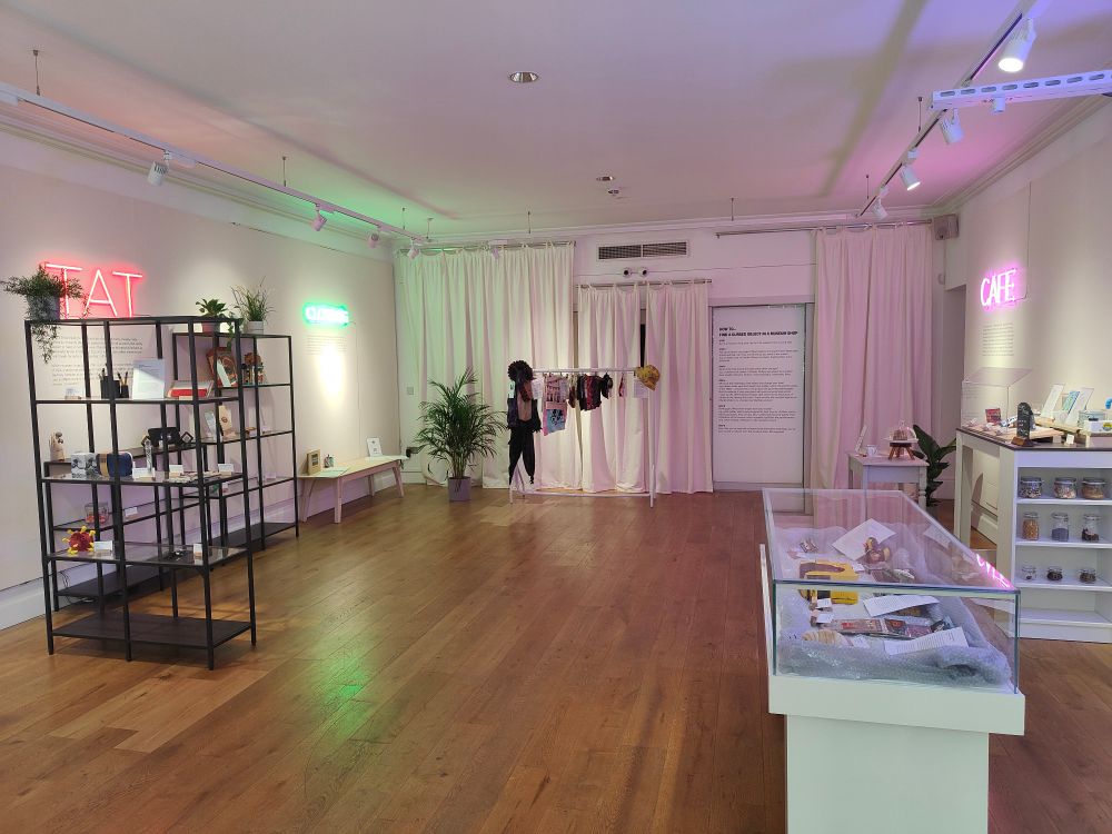 Art gallery with wooden flooring, small black shelving with objects and a white museum display case with glass top. Sign on left wall says Tat, on right wall Café. 