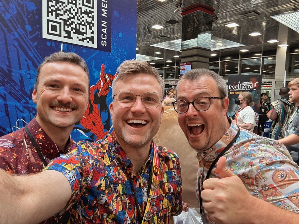 Three men in colorful shirts, smiling, with one giving a thumbs up. 