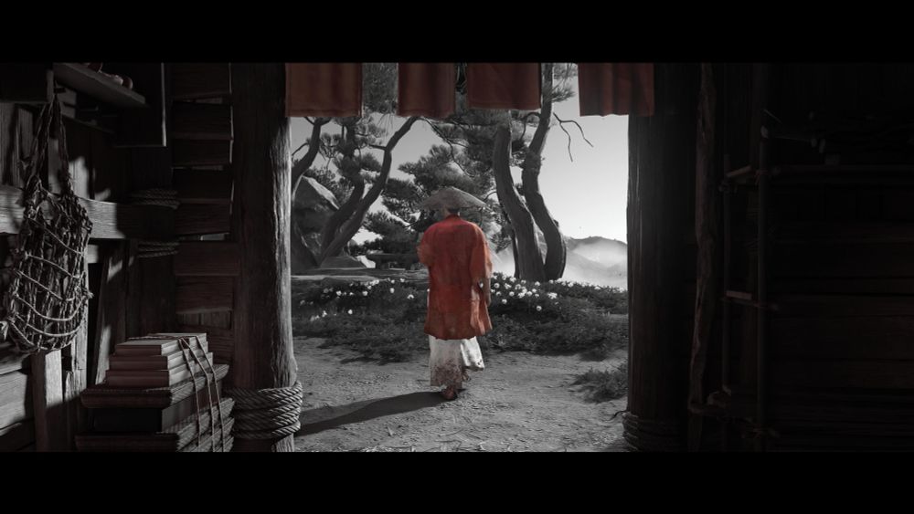 A man in a red cloak walks out of a darkened hut into bright sunlight. 