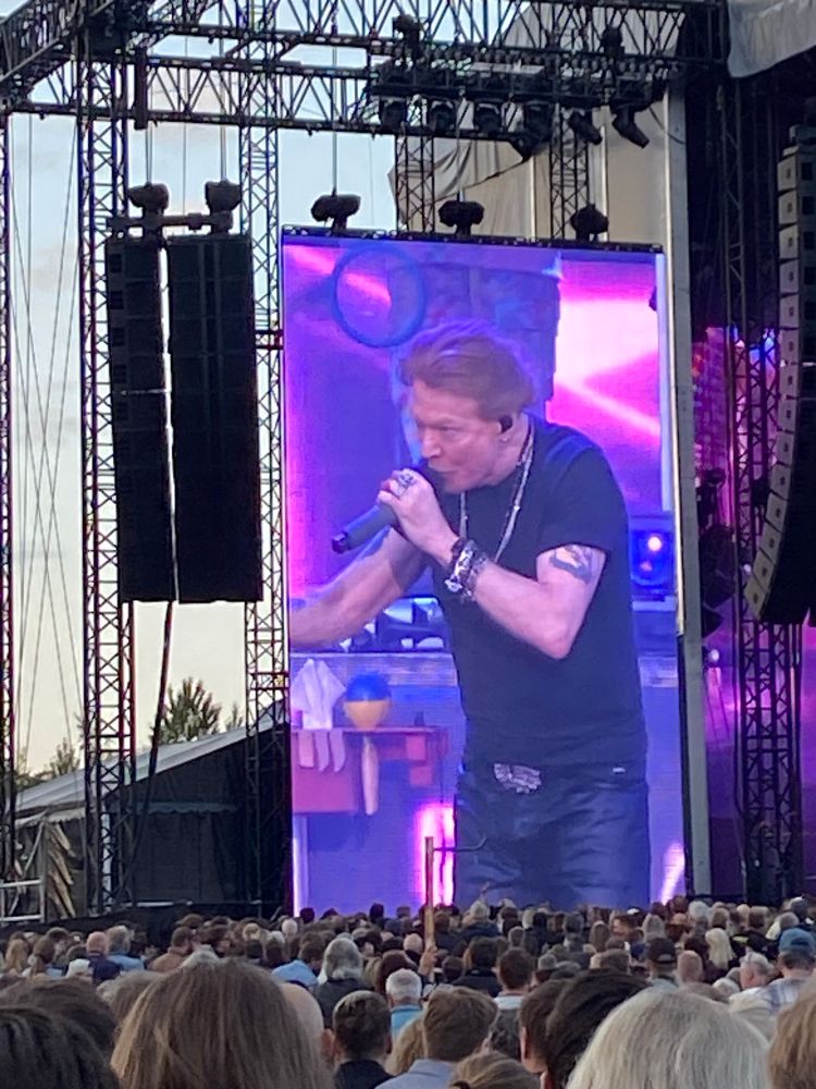 A picture of Axl Rose on a big screen during a concert. In the background on a table you can see a distinct blue and yellow sphere on the table behind him. Showing support for Ukraine