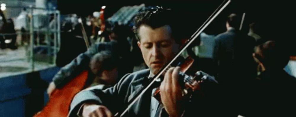 a man in a tuxedo is playing a violin in front of a crowd